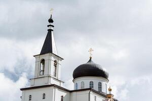 a ortodoxo Igreja é branco contra a céu, uma Sombrio cúpula em topo carrinhos uma dourado cruzar, uma campanário com sinos. foto