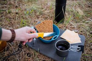 acampamento turista Comida mentiras em uma pequeno mesa, cozinhar sanduíches dentro natureza, cortar pão com uma faca, acampamento equipamento, turista faca, viagem comida, chá dentro uma caneca. foto