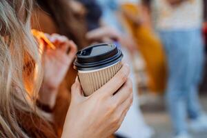 uma mão detém uma vidro do café dentro uma construir pacote, uma menina bebidas uma quente beber em a rua, uma rápido refeição em a rua, uma lanche em a estrada, uma copo do chá dentro dela mão. foto