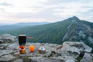 café da manhã do uma turista em uma montanha declive, uma conjunto do pratos para cozinhando dentro natureza em uma caminhada. laranja chá caneca. foto