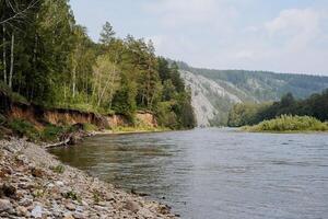 uma calma rio fluxos entre a montanhas, a natureza do Rússia é a república do bascortostão, uma branco rio, uma argila íngreme banco, uma Rocha dentro a distância em a horizonte. foto