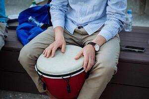 uma hipster dentro uma camisa tocam a africano tambor em a esperando sala, étnico música em a ruas do a cidade, etno sons em uma percussão instrumento. foto