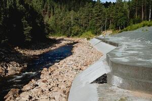 a barragem é protetora em uma montanha rio, uma fortificado estrutura fez do concreto, proteção do a costa a partir de erosão, montanha água fluxo, ampla pedras dentro a leito do rio. foto