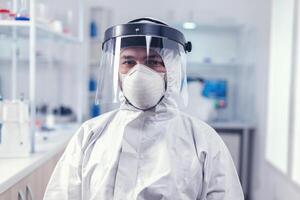 bioquímica cientista vestindo face mascarar e face escudo Como segurança precaução para covid19 surto trabalhando dentro laboratório. sobrecarregado investigador vestido dentro protetora terno contra invectiva com coronavírus durante global epidemia. foto