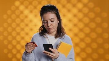 mulher segurando livros, compra Mais com telefone, transmitindo alegria do lendo conceito, estúdio fundo. pessoa comprando romances conectados com crédito cartão, mostrando apreciação para literatura, Câmera b foto