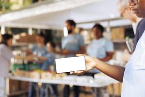 Preto mulher segurando uma celular com isolado brincar modelo para personalizadas mensagens relacionado para caridade. africano americano fêmea voluntários ganancioso digital dispositivo com em branco branco tela mostrar. foto