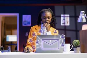 africano americano mulher trabalhando em computador portátil, enviando e-mails para o negócio parceiros, conectados conectividade conceito. controlo remoto trabalhador usando xr aumentado realidade tecnologia para interagir com caderno tela foto