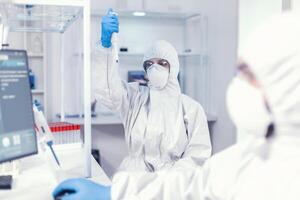 trabalhando com micropipeta usando proteção terno Como segurança precaução para coroavírus. equipe do microbiologistas dentro pesquisa laboratório conduzindo experimentar durante global pandemia com COVID-19. foto