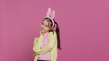 sorridente pequeno menina sonhando sobre presentes e Comida para Páscoa domingo celebração, sentindo-me animado sobre Primavera feriado. jovem criança com Coelho orelhas posando contra Rosa fundo. Câmera uma. foto