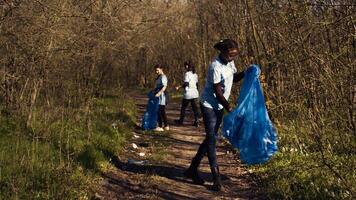 grupo do diverso ativistas colheita acima a Lixo e plástico desperdício, colecionar e reciclando lixo dentro a madeiras. pessoas fazendo voluntário trabalhos para limpar \ limpo a natural habitat. Câmera b. foto