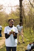 africano americano voluntário apresenta uma vegetação plantinha com orgânico solo, preservando natureza e brigando poluição. orgulhoso jovem menina fazendo voluntário trabalhos para crescer árvores, Salve  a planeta. foto