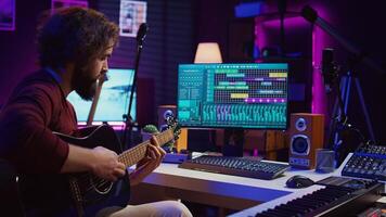 musical artista gravação guitarra sons para uma Novo rastrear dentro casa estúdio, mesa de som controles e amanhecer Programas em computador. jovem músico jogando acústico instrumento, música indústria. Câmera b. foto