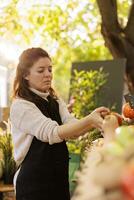 fêmea pequeno o negócio proprietário arranjo localmente crescido orgânico produzir em agricultores mercado cabine. jovem mulher fornecedor colocando fresco frutas e legumes em mercado verde ficar em pé, pronto para vender para clientes. foto