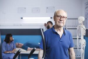 retrato do aposentado paciente visitando fisica terapia Centro. Senior velho homem olhando às a Câmera, preparando para recuperar através da exercício e ginástica às uma reabilitação tratamento clínica. foto