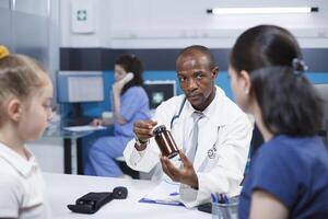 mãe e filha consultar com uma cuidados de saúde profissional sobre seus preocupações. africano americano médico explica tratamento e diagnóstico para caucasiano pacientes enquanto segurando medicação garrafa. foto