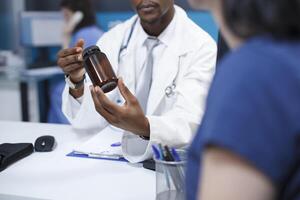 fechar-se tiro do a africano americano médico descrevendo a diagnóstico e curso do tratamento do uma caucasiano paciente enquanto segurando uma garrafa do medicamento. uma mulher recebendo médico conselho. foto