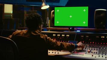 africano americano audio engenheiro usa tela verde em pc dentro profissional gravação estúdio, trabalhando com mistura console e torção botões para editar faixas. música produtor criando músicas. Câmera b. foto