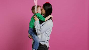 fofa mãe e criança mostrando amor para cada de outros dentro estúdio, mãe abraçando e se beijando dela pequeno criança pequena filho com Coelho ouvidos. adorável pequeno família rindo juntos e tendo Diversão. Câmera b. foto