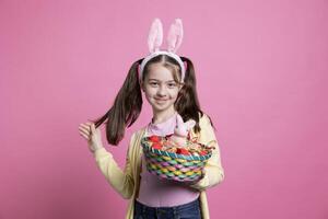 pequeno criança com Coelho orelhas detém Páscoa brinquedos e decorações, evocando a encantamento do a temporada. fofa menina com adorável sorrir mostrando uma Coelho e ovos dentro uma cesta em Câmera. foto