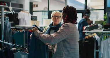 africano americano varejo escriturário mostrando Novo moda coleção para Senior cliente dentro departamento loja às a shopping center. grávida assistente fazer cor sugestões para regular cliente, consumismo. Câmera b. foto