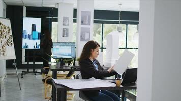 arquitetônico técnico examina 3d construção modelo dentro criativo agência coworking espaço, levando notas do Projeto linhas e Medidas. mulher medindo maquete escala e elementos. tripé tomada. foto