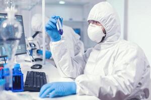 médico conduzindo científico vírus pesquisa segurando teste tubo. vestindo ppe terno. cientista dentro laboratório vestindo macacão fazendo pesquisa e analisando substância durante global pandemia com COVID-19. foto