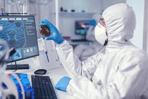 médico cientista segurando petri prato estudando vírus amostra vestido dentro bacteriológico terno médicos analisando vacina evolução usando Alto tecnologia pesquisando diagnóstico contra covid19 vírus. foto