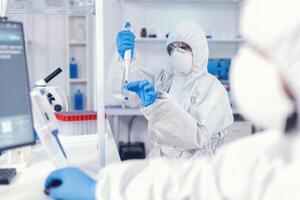 cuidados de saúde médico levando amostra a partir de teste tubo usando micropipeta. equipe do microbiologistas dentro pesquisa laboratório conduzindo experimentar durante global pandemia com COVID-19. foto