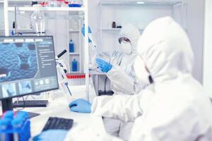 com experiência médico levando amostra a partir de teste tubo usando micropipeta vestindo estéril terno. equipe do microbiologistas dentro pesquisa laboratório conduzindo experimentar durante global pandemia com COVID-19. foto