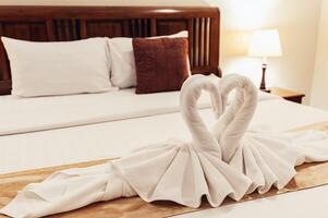 branco chocalhos estavam enrolado juntos dentro a forma do uma cisne e colocada em uma colchão em uma de madeira cama com lâmpadas em qualquer lado do a cama. foto
