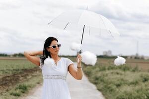 mulher é segurando uma branco guarda-chuva e cercado de algodão nuvens foto