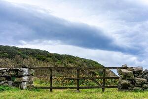 velho de madeira portão fechamento uma típica açoriano pedra parede contra uma pano de fundo do tormentoso nuvens, promissor chuva. foto