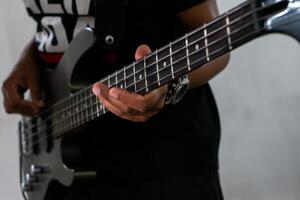 uma homem jogando uma graves guitarra dentro uma casual contexto. ele é focado em dele instrumento, dedos planador sobre a cordas. dele relaxado postura e casual vestuário sugerir uma descontraído música sessão. foto