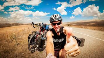 inspirado Smartphone selfie retrato animado alegre caucasiano masculino ciclista mostrar polegares acima de bicicleta olhando para Câmera risonho face. viagem por aí a mundo de bicicleta foto