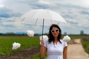 mulher é segurando uma branco guarda-chuva e cercado de algodão nuvens foto