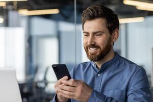 fechar-se foto do uma cansado jovem homem sentado às dele escrivaninha dentro a escritório e usando uma Móvel telefone.