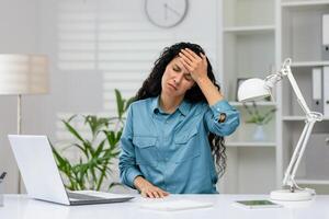 frustrado profissional fêmea experimentando estresse e dor de cabeça enquanto trabalhando em uma computador portátil dentro uma moderno escritório contexto. foto