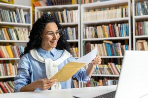 uma alegre mulher vestindo óculos lê uma postal mensagem com uma sorriso, cercado de estantes de livros dentro uma biblioteca. foto