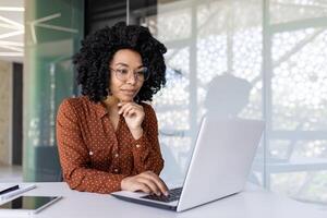 sério pensando mulher trabalhando com computador portátil, digitando em teclado, pensando concentradamente sobre resolução atual problemas, o negócio mulher bem sucedido satisfeito e confiante às local de trabalho dentro escritório. foto