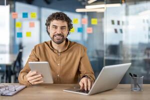 a escritório configuração com uma profissional usando uma computador portátil e uma tábua simultaneamente, representando multitarefa e eficiência dentro uma moderno ambiente de trabalho. foto