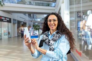 compras em uma viagem. jovem hispânico mulher é viajando, compras dentro uma supermercado, segurando uma telefone foto