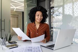 jovem bem sucedido financista trabalho com documentos e contratos dentro a escritório, satisfeito com a resultados do financeiro Atividades, empresária avaliações contas, relatórios e contratos, computador portátil. foto