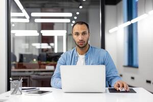 focado masculino profissional usando uma computador portátil às uma moderno área de trabalho, incorporando determinação e eficiência. foto