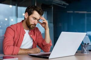 frustrado homem de negocios depressivo às local de trabalho trabalhando em computador portátil, homem dentro camisa chateado e triste descontente com mau trabalhos resultados e realização dentro escritório. foto