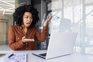 a africano americano empresária mostra frustração e raiva às dela computador dentro uma moderno escritório ambiente, expressando local de trabalho estresse. foto