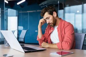 frustrado homem de negocios depressivo às local de trabalho trabalhando em computador portátil, homem dentro camisa chateado e triste descontente com mau trabalhos resultados e realização dentro escritório. foto