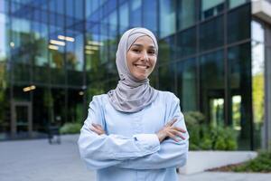 profissional jovem muçulmano mulher com uma radiante sorriso, vestindo uma hijab, em pé com confiança lado de fora a escritório. foto
