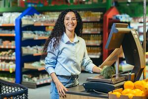 retrato do uma feliz mulher comprador dentro uma supermercado, uma hispânico mulher pesa brócolis repolho em uma escala, sorrisos e parece às a Câmera, dentro uma loja entre prateleiras com mercearia produtos foto