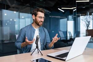 o negócio treinador dentro escritório gravação audio podcast, homem de negocios trabalhando às computador portátil usando profissional microfone e computador portátil para conectados rádio, e Treinamento controlo remoto. foto