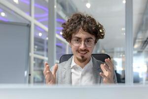 uma cabelo encaracolado jovem homem de negocios focos em uma discussão enquanto trabalhando dentro uma moderno escritório ambiente, incorporando corporativo determinação. foto